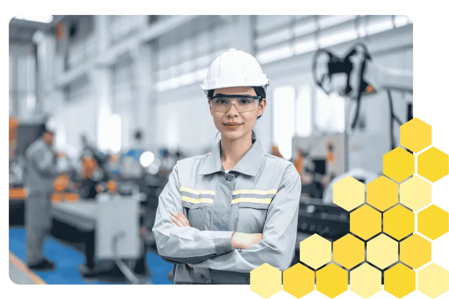 Female engineer wearing safety gear standing confidently in manufacturing facility with machinery in background