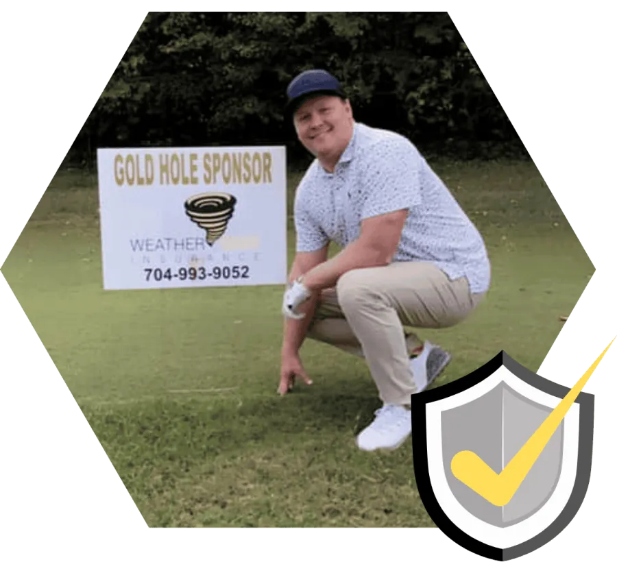 Smiling man in golf attire crouches near a sign for Gold Hole Sponsor on a green golf course.