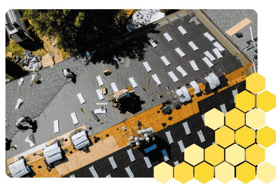 Aerial view of workers installing black roofing felt with white strips on a pitched roof under sunny conditions.