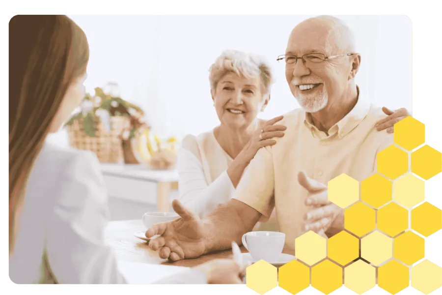 Senior couple smiling and talking with a healthcare professional in a bright, cozy kitchen setting.