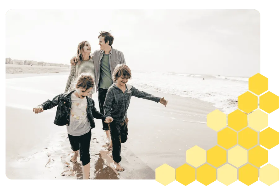 Happy family of four walking barefoot on the beach enjoying a sunny day together by the sea.