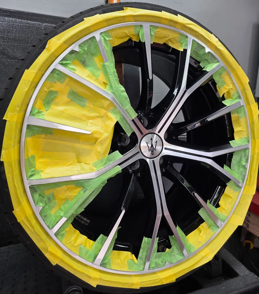 Close-up of a Maserati wheel rim masked with yellow and green tape for painting or protection.
