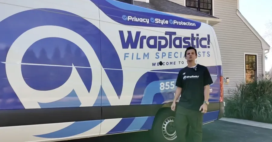 Man standing next to a WrapTastic van with bold blue and white branding outside a residential house.