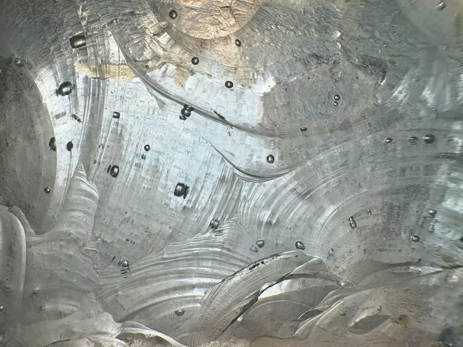 Close-up of textured and translucent ice with smooth curves and embedded air bubbles, reflecting light.