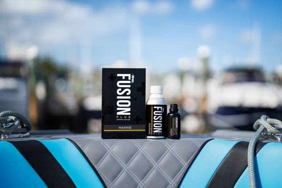 Fusion Plus marine ceramic coating products displayed on a quilted boat seat with blurred marina background.
