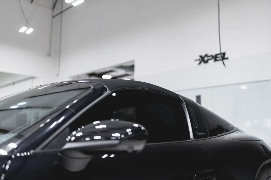 Close-up of black sports car side with tinted windows and sleek design in showroom with XPEL logo