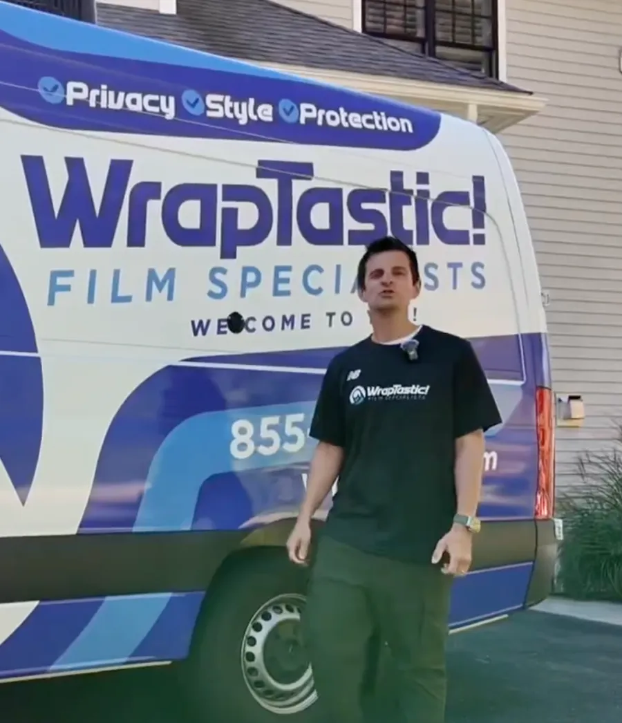 Man standing next to a Wraptastic van with large blue and white branding in a residential area.