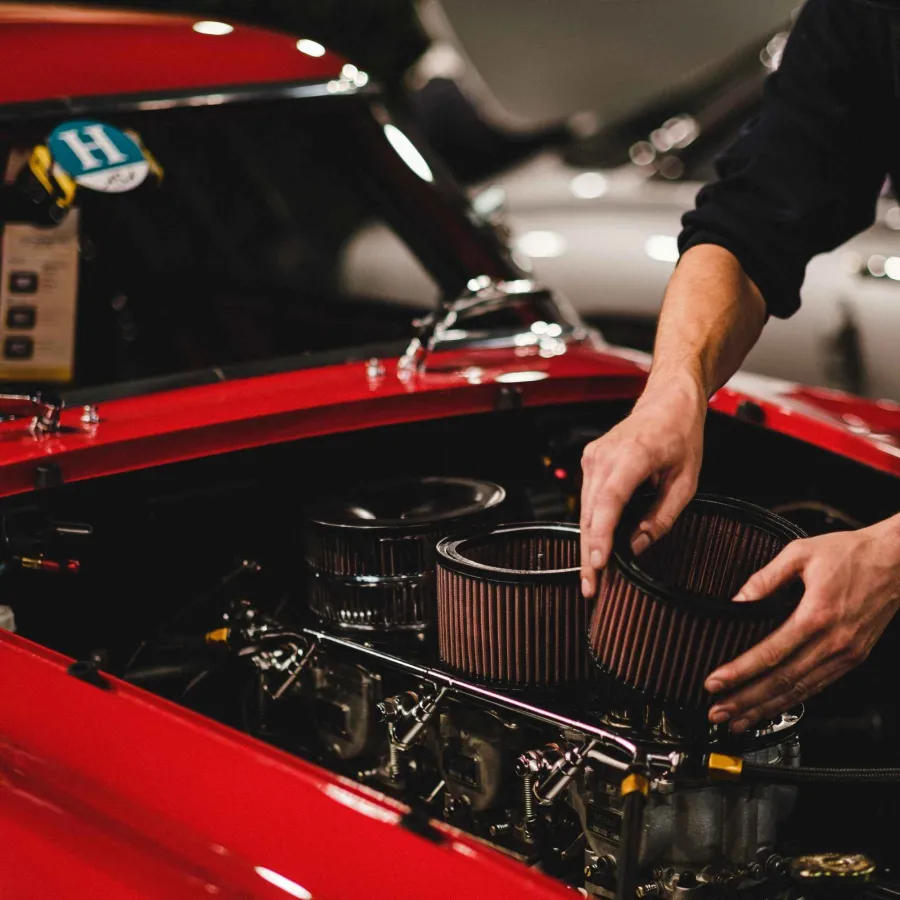 Mechanic hands installing or removing air filters on a red vintage car engine with detailed components.