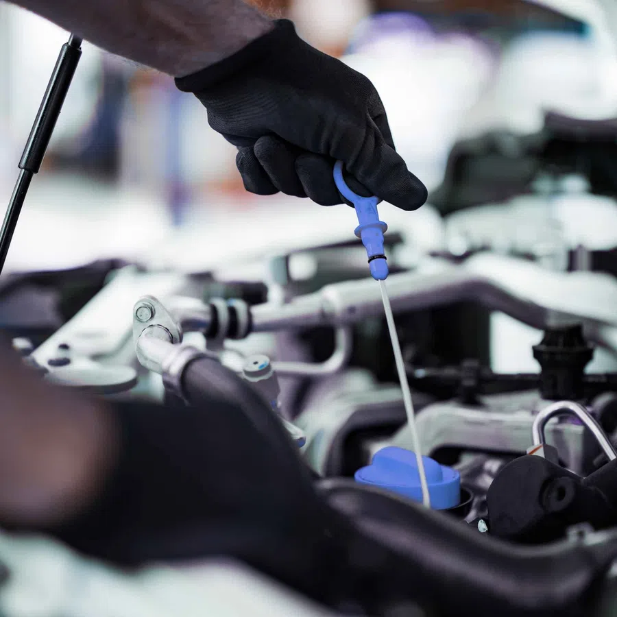 Gloved hand pulling engine oil dipstick from car engine for checking oil level during maintenance.
