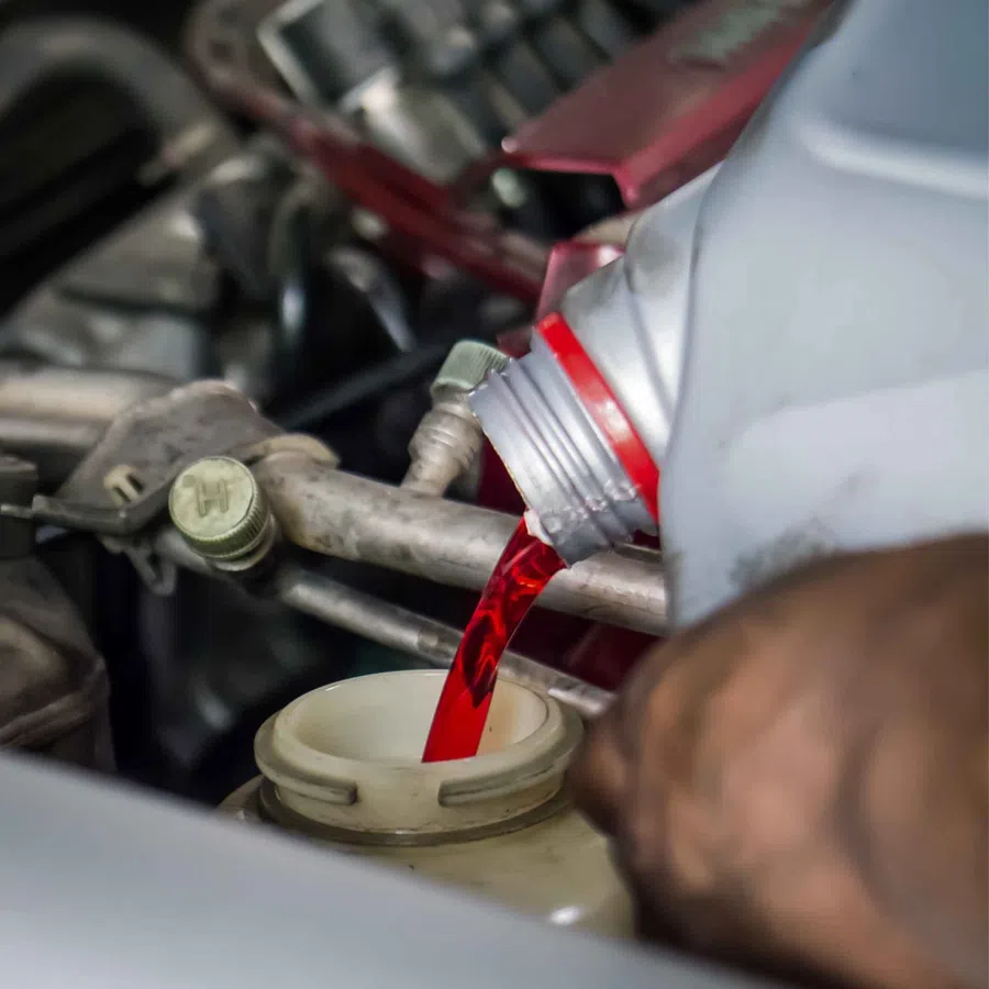 Red automotive fluid being poured into a vehicle reservoir during maintenance or repair work.