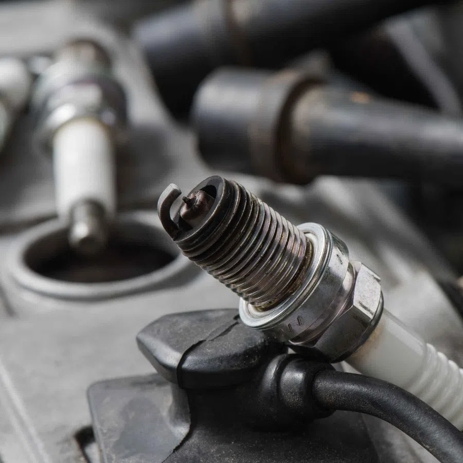Close-up of a used car spark plug resting on an engine component with other spark plugs blurred in background