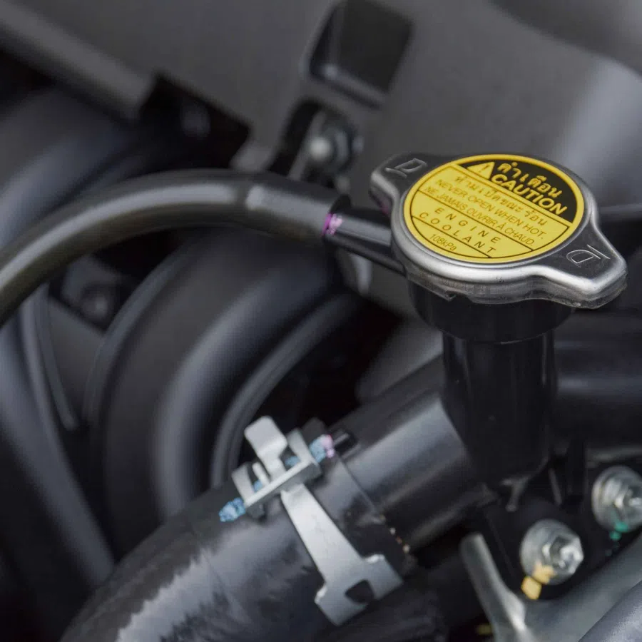 Close-up of a car engine coolant reservoir cap with warning label and connected hose.