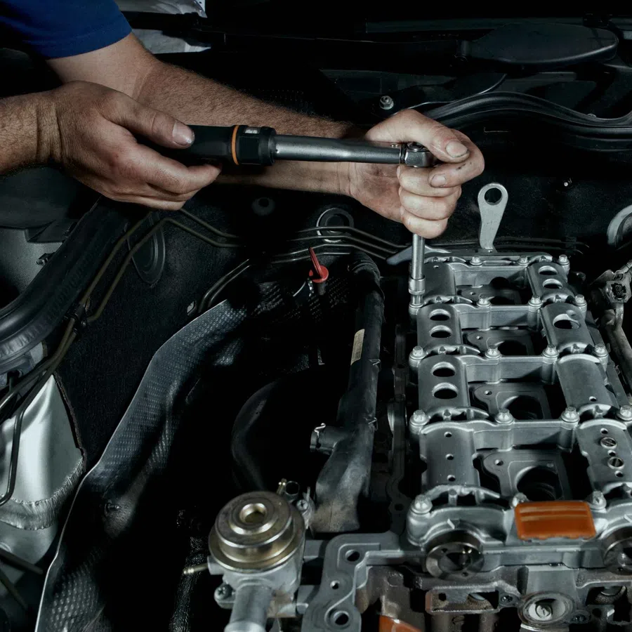 Mechanic using a torque wrench to tighten bolts on a car engine in a close-up shot under the hood.
