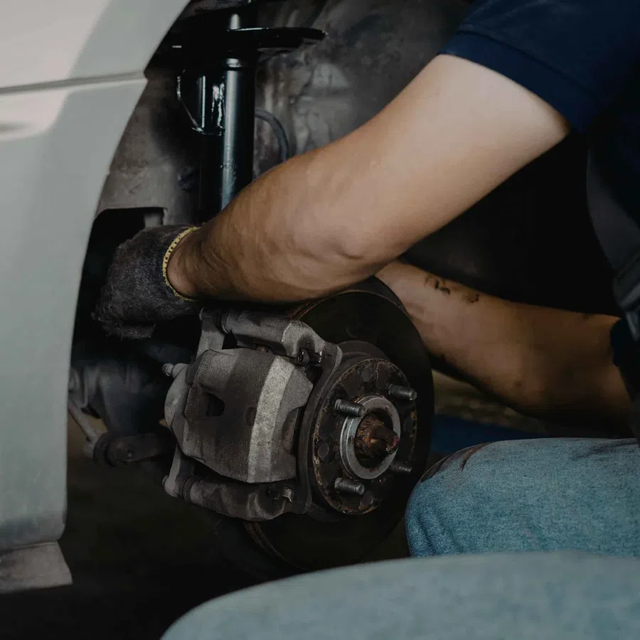 Mechanic repairing a car's brake system, focusing on the brake disc and caliper with hands at work.