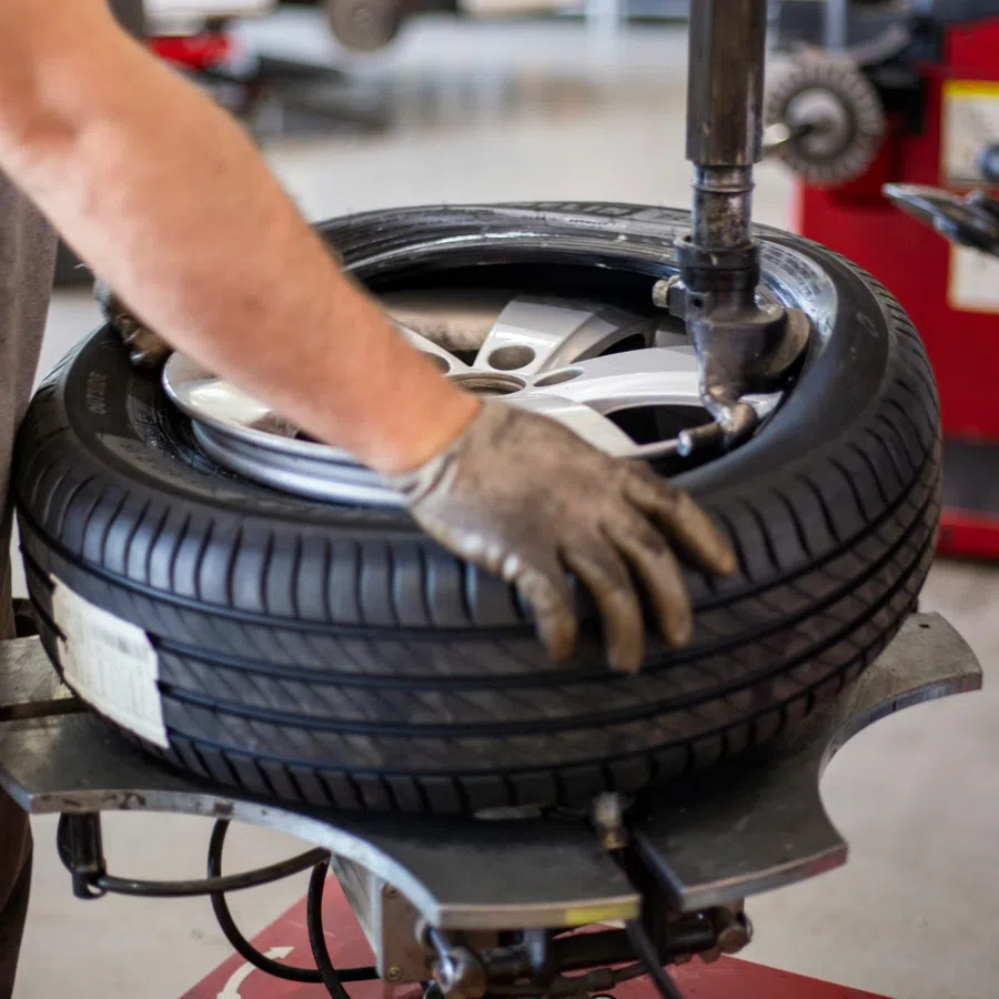 Mechanic uses tire changing machine to mount a tire on a rim in an auto repair shop with white car in background